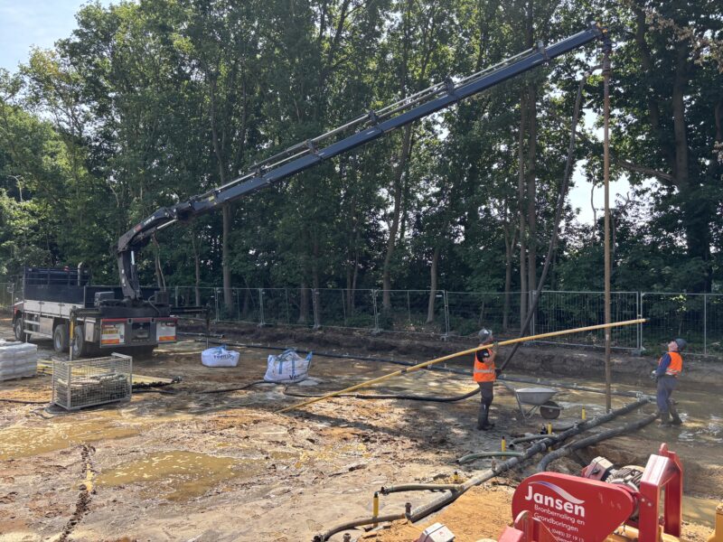 Twee medewerkers van InnoTherm voeren grondboringen uit op een bouwplaats met een kraanwagen en een pomp van Jansen Bronbemaling.